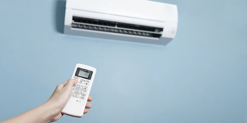 air conditioner cost - how much does an air conditioner cost - air conditioner mouted on wall with hand holding remote control