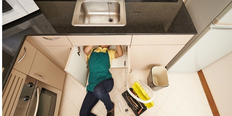 gurgle - fix kitchen sink - person on floor working on undersink plumbing
