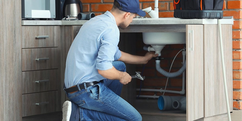 gurgling kitchen sink - What Should You Do about a Gurgling Noise Coming from Your Kitchen Sink? - plumber inspecting pipes under kitchen sink
